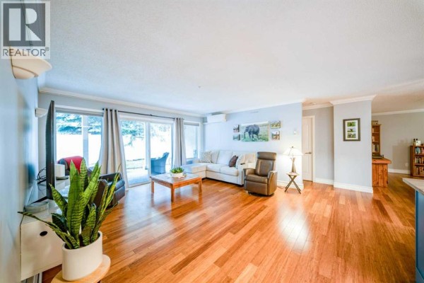 Living room featuring a sectional sofa, recliner, coffee table, and sliding glass doors. - 2107, 20 Harvest Rose Park Ne, Calgary