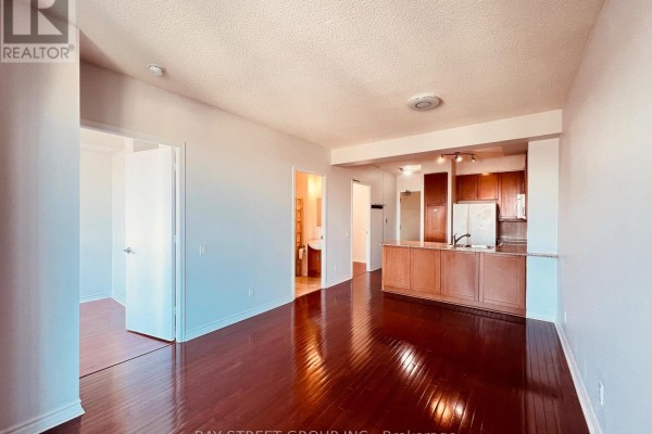 Living room with dark hardwood floors opening to a kitchen and bathroom. - 2107 - 60 Byng Avenue, Toronto