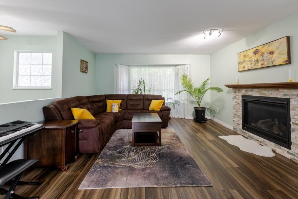 Living room with a brown sectional sofa, a stone-faced fireplace, and wood-look flooring. - 21073 93 Avenue, Langley