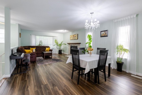 Open-concept living and dining area with a table set for six, a sectional sofa, and wood-look flooring. - 21073 93 Avenue, Langley