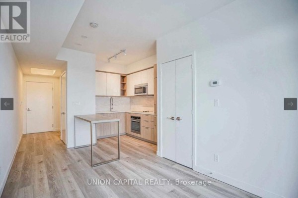 Apartment living area and kitchen with white walls, light wood floors, and modern cabinetry. - 2108 - 50 Ordnance Street, Toronto