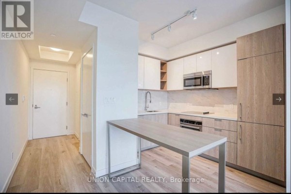 Open concept apartment showing a kitchen with light wood and white cabinets and a small dining table. - 2108 - 50 Ordnance Street, Toronto