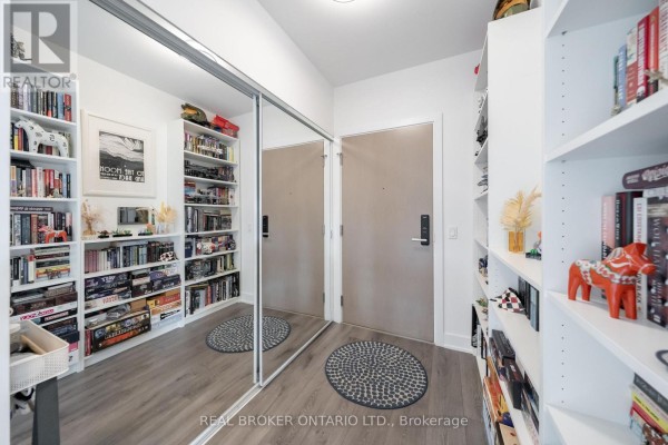 Hallway with floor-to-ceiling mirrored closet doors and white bookshelves filled with books. - 2108 - 575 Bloor Street E, Toronto