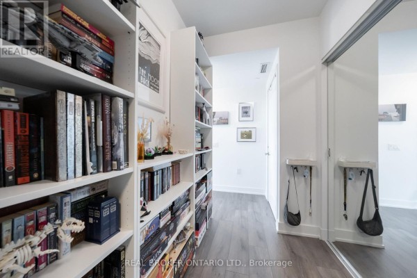 Apartment hallway with white bookshelves, artwork on wall, and key hooks by door. - 2108 - 575 Bloor Street E, Toronto