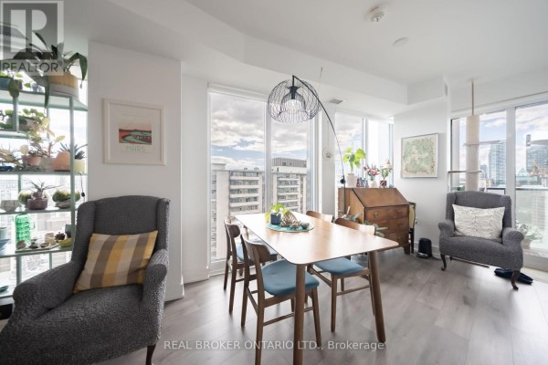 Dining area with wooden table, four blue chairs, two grey armchairs, and city view windows. - 2108 - 575 Bloor Street E, Toronto