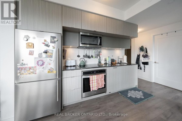 Kitchen with stainless steel refrigerator, grey cabinets, dark countertop, oven, and microwave. - 2108 - 575 Bloor Street E, Toronto