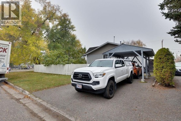 White pickup truck parked under a carport next to a duplex exterior. - 2108 6th Avenue, Prince George