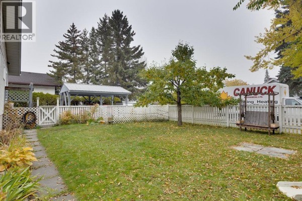 Backyard view of a duplex with a grassy lawn, white picket fence, and trees. - 2108 6th Avenue, Prince George