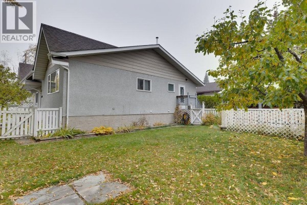 Side view of the duplex backyard with a white fence and mature trees. - 2108 6th Avenue, Prince George