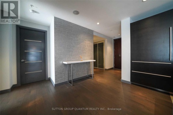 Apartment entryway with dark wood floors, grey textured wallpaper, and dark wood doors. - 2109 - 180 University Avenue, Toronto