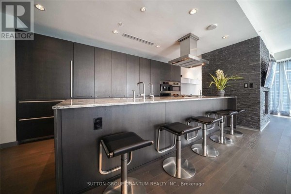 Modern kitchen with dark wood cabinets, marble island with bar stools, and stainless steel appliances. - 2109 - 180 University Avenue, Toronto