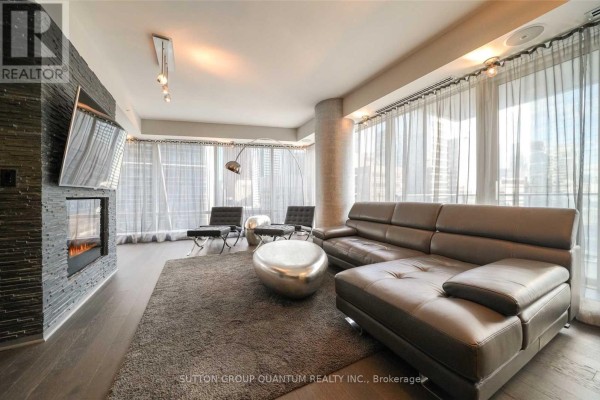 Living room with dark leather sectional, fireplace, floor-to-ceiling sheer curtains, and metallic coffee table. - 2109 - 180 University Avenue, Toronto