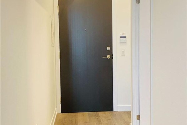 Apartment entrance with a dark grey door and light brown wood-look flooring. - 211 - 10 Honeycrisp Crescent, Vaughan