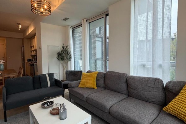 Living room with a grey sofa, white coffee table, and sheer curtains covering large windows. - 211 - 150 Fairview Mall Drive, Toronto