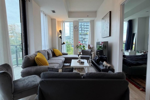 Living room with grey sofas, white coffee table, TV, and view into the bedroom. - 211 - 150 Fairview Mall Drive, Toronto