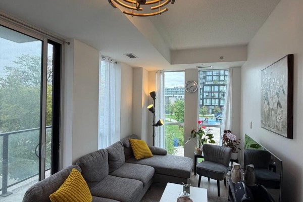 Living room featuring a grey sectional sofa, floor lamp, and a view of trees and buildings. - 211 - 150 Fairview Mall Drive, Toronto