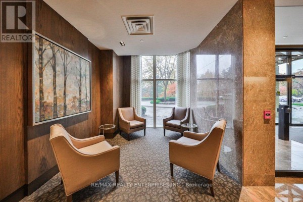 Cozy seating area with four beige chairs, side tables, and abstract art on a wood-paneled wall. - 211 - 1800 The Collegeway, Mississauga