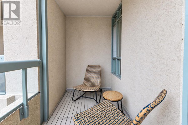 Small balcony with two wicker chairs and a side table, facing a building wall. - 211 - 35 Merton Street, Toronto