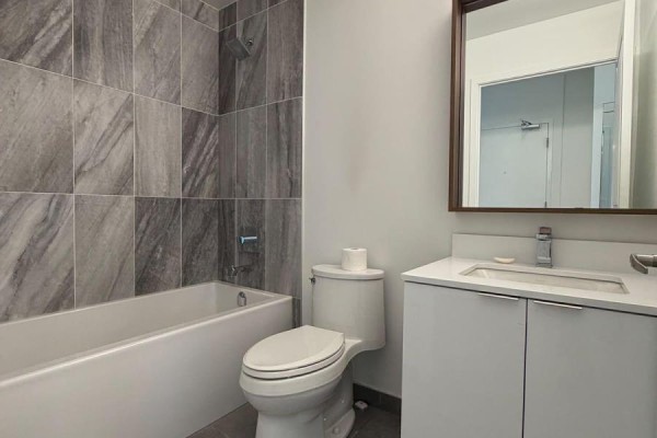 Bathroom with white tub, grey marble tiled walls, toilet, and vanity. - 211 - 543 Richmond Street W, Toronto