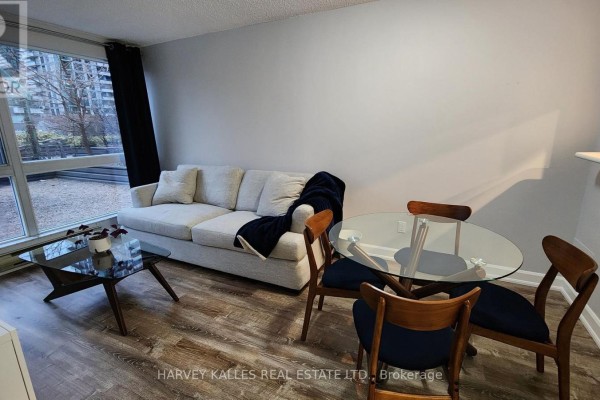 Living and dining area with light grey sofa, round glass table, and large window view. - 211 - 7 Broadway Avenue, Toronto