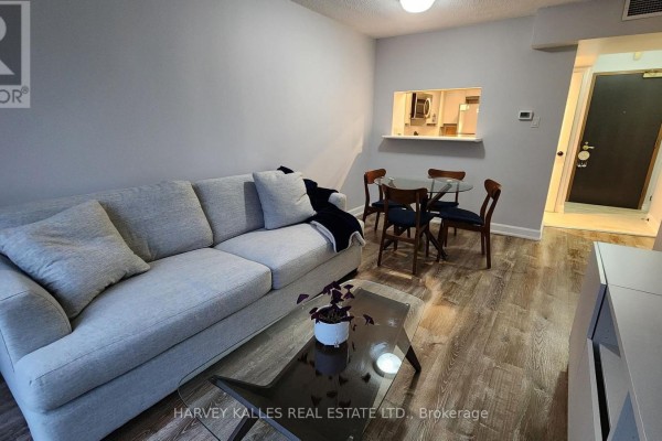 Living room showing sofa, dining set, pass-through to kitchen, and hallway to front door. - 211 - 7 Broadway Avenue, Toronto