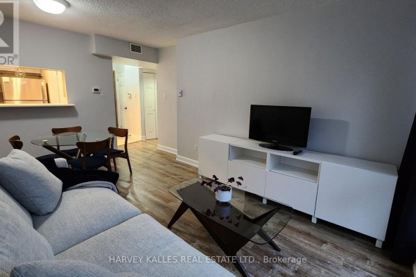 Living area with sofa, coffee table, TV console, and dining set visible from hallway. - 211 - 7 Broadway Avenue, Toronto