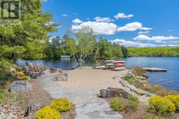 Sandy beach area with Muskoka chairs, canoes, and a dock on the lake. - 211 - 727 Grandview Drive, Huntsville
