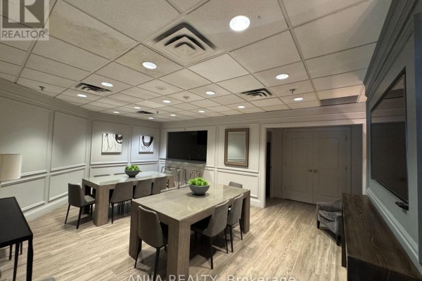 Communal lounge area with two large tables, chairs, televisions, and wooden flooring. - 211 - 75 York Mills Road, Toronto