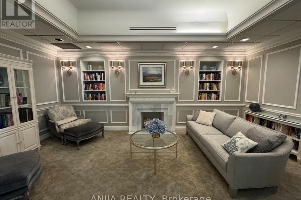 Library-style lounge with a sofa, armchair, fireplace, built-in bookshelves, and a china cabinet. - 211 - 75 York Mills Road, Toronto