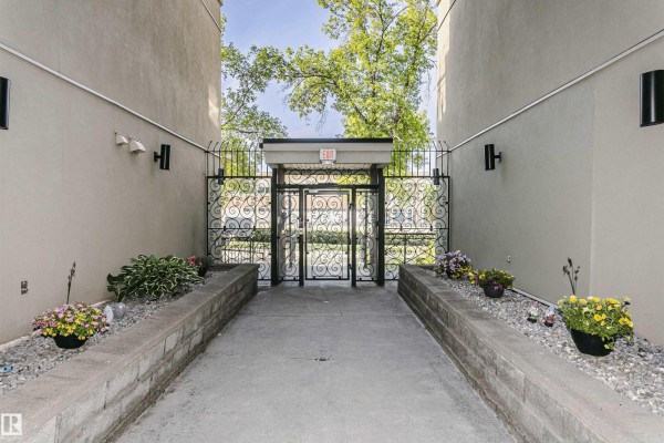 Walkway leading to the building's entrance with a modern glass elevator shaft and exterior walls. - #211 10808 71 Av Nw, Edmonton