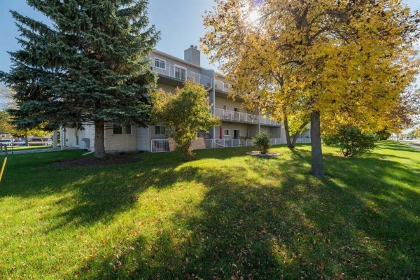 Exterior view of apartment building with green lawn and trees in autumn. - 211 1683 Plessis Road, Winnipeg