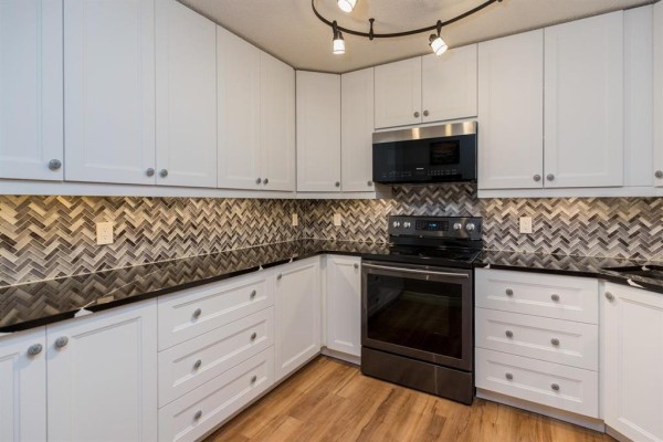 Corner kitchen with white cabinets, granite countertops, and stainless steel appliances. - 211 1683 Plessis Road, Winnipeg