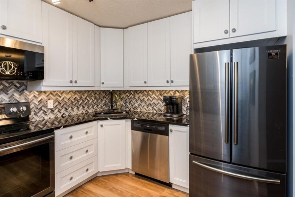 Corner kitchen with white cabinets, granite countertops, and stainless steel appliances. - 211 1683 Plessis Road, Winnipeg