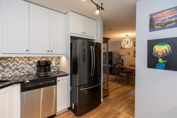 View of kitchen and dining area with wood floors and modern light fixtures. - 211 1683 Plessis Road, Winnipeg