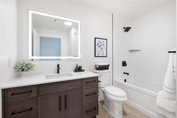 Bathroom with a dark wood vanity, white countertop, illuminated mirror, toilet, and bathtub. - 211 1924 St. Mary's Road, Winnipeg