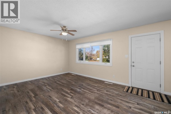 Living room with beige walls, wood-look vinyl plank flooring, a ceiling fan, and a front door. - 211 31st Street E, Prince Albert