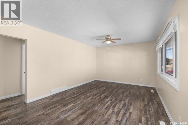 Living room showing beige walls, wood-look vinyl plank flooring, a ceiling fan, and a doorway to the left. - 211 31st Street E, Prince Albert