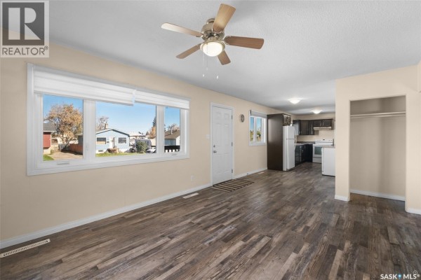 Living room with beige walls, wood-look vinyl plank flooring, a ceiling fan, and view of the open concept kitchen. - 211 31st Street E, Prince Albert