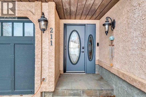 Close-up of the front entrance with a gray double door, oval glass inlays, and house number 211. - 211 4 Avenue Se, Three Hills