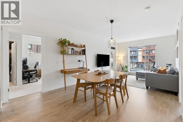 Dining area with wooden table, bookshelf, and living room view through large window - 211 625 E 3rd Street, North Vancouver