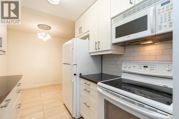 Interior hallway with white walls, black front door, and light wood-look flooring. - 211 9101 Horne Street, Burnaby