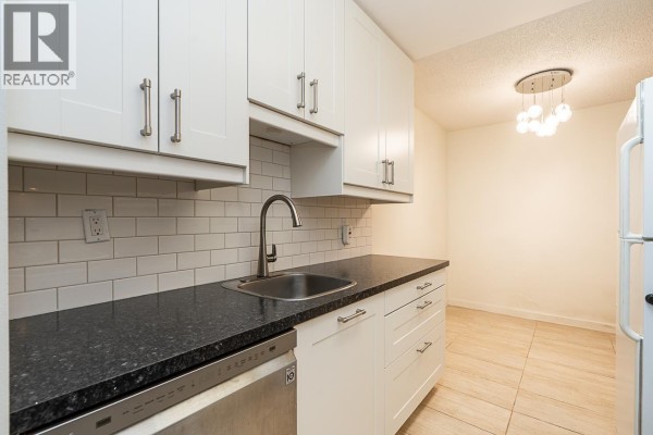Apartment kitchen with white cabinets, white appliances, and tiled flooring, opens to living area. - 211 9101 Horne Street, Burnaby