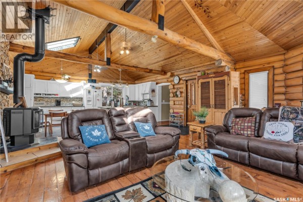 Living area with log walls, vaulted wood ceiling, wood-burning stove, and open kitchen view. - 211 Al Drive, Turtle Lake
