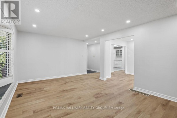 Living room with light wood floors, white walls, recessed lighting, and archway to the kitchen. - 211 Harcourt Avenue, Ottawa