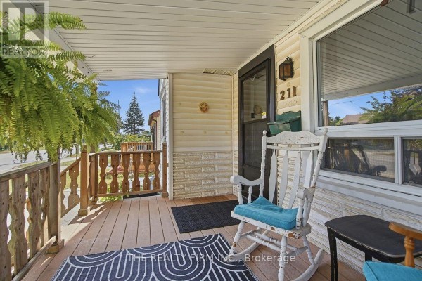 Close-up of a covered front porch with wooden floorboards, a rocking chair, and a rug. - 211 Highbury Avenue N, London East