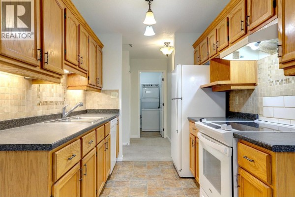 Kitchen with oak cabinets, beige tile backsplash, stainless steel sink, and white appliances. - 211 Kildonan Avenue Unit# 212, Enderby