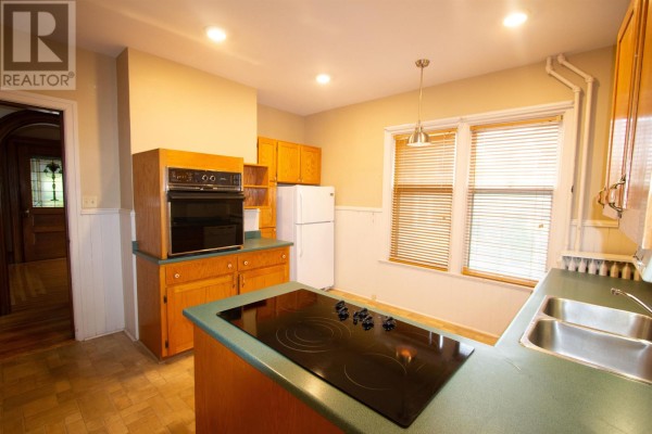 A kitchen with light wood cabinets, green countertops, and black stovetop. - 211 Notre Dame Street, Summerside