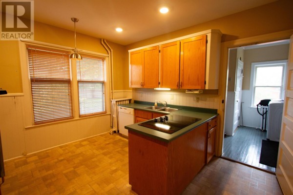 A kitchen with light wood cabinets, green countertops, and a view into a laundry area. - 211 Notre Dame Street, Summerside