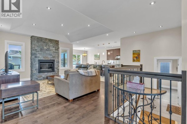 Living room with stone fireplace, leather sofa, armchair, TV, and large window views. - 211 Robson, Leamington