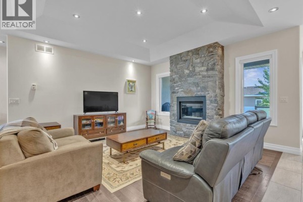 Open-concept living area showing a gray leather sofa, dining area, and dark wood kitchen cabinets. - 211 Robson, Leamington